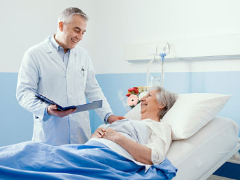 Picture of male medical provider tending to a female patient, who is lying in a hospital bed.
